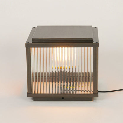 Modern outdoor wall or pillar light with ribbed glass and metal frame on neutral background creating warm ambient exterior lighting.