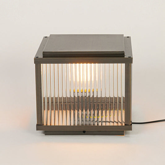 Modern outdoor wall or pillar light with ribbed glass and metal frame on neutral background creating warm ambient exterior lighting.