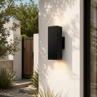 Minimalist black aluminum rectangular up down wall sconce on white stucco facade for modern outdoor entryway lighting.