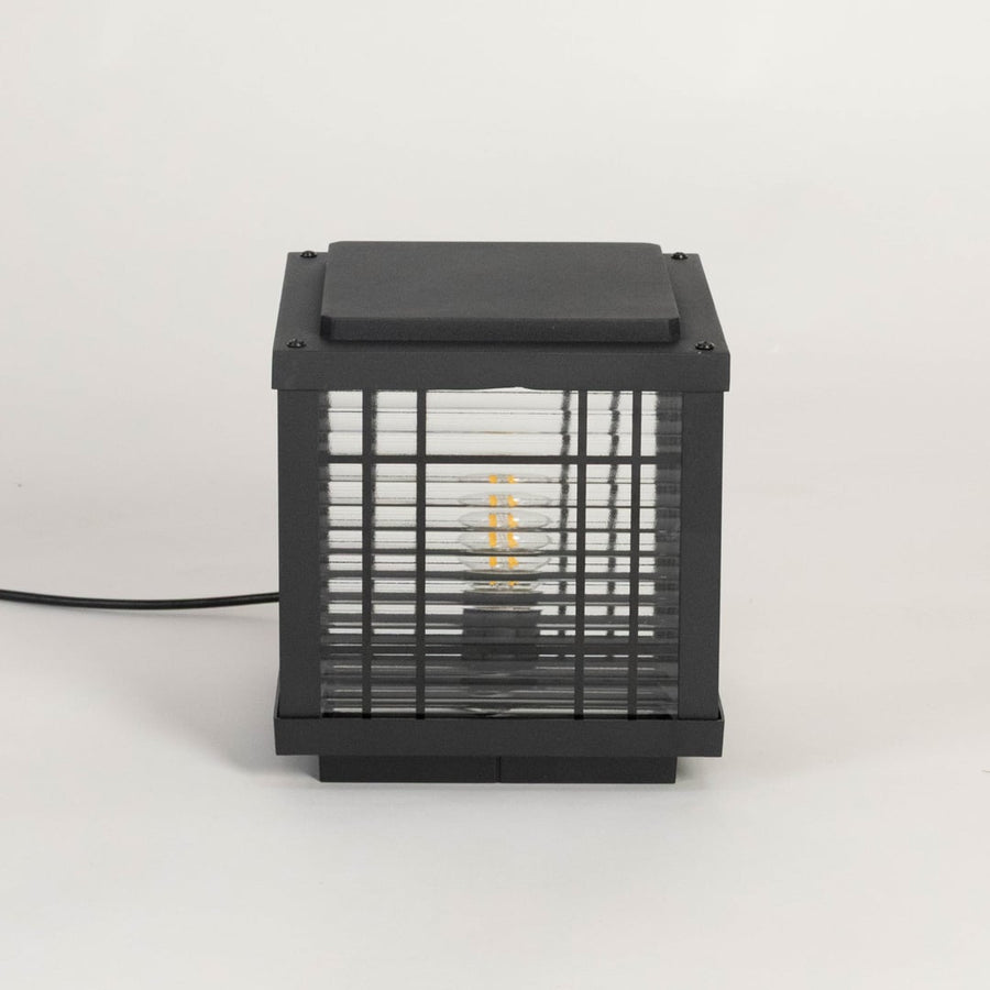 Black outdoor pillar lamp glowing LED through frosted glass ideal for garden patio balcony and modern exterior lighting.