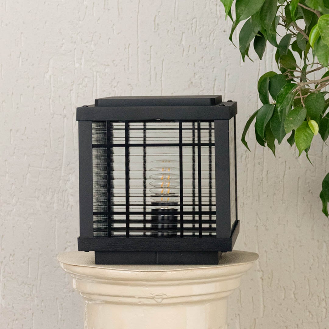Square pillar light placed on an off white pedestal featuring metal grid detailing and glass sides presented as a dimension image highlighting proportions.