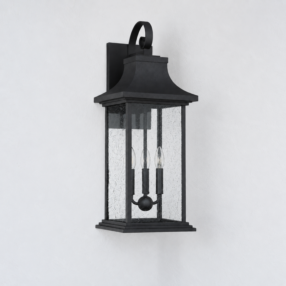 A black outdoor wall lantern light fixture with textured clear glass panels and two candle-style bulbs, mounted against a plain white wall.