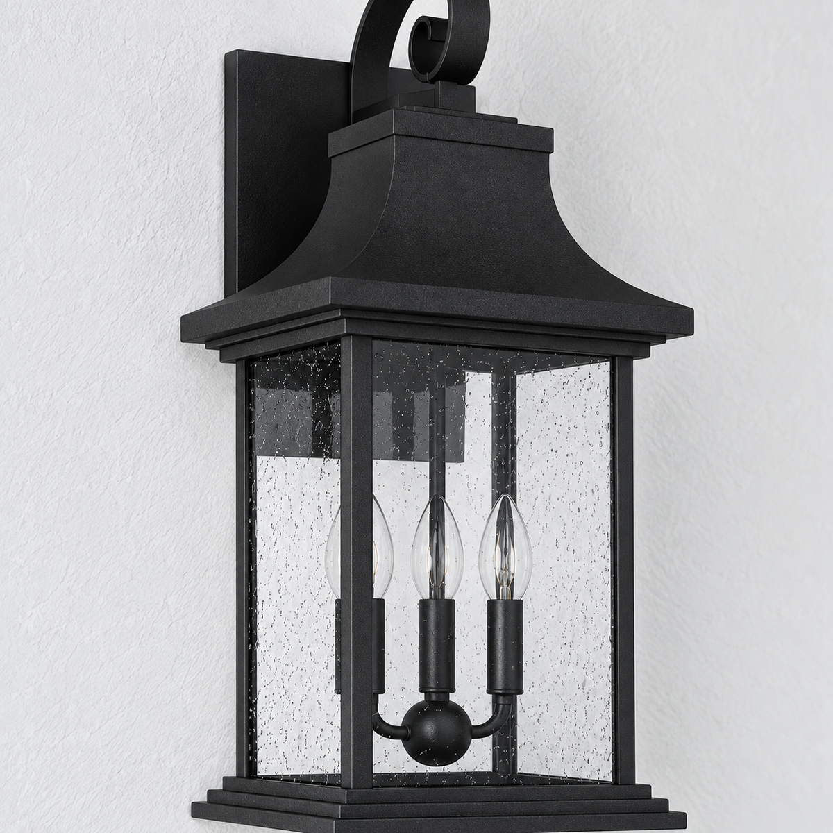 A black outdoor wall sconce with a textured glass panel and three visible light bulbs, mounted against a white textured wall.