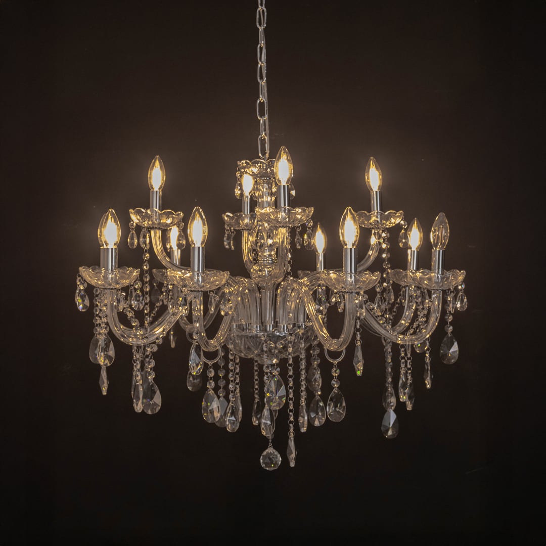 Crystal chandelier with candle lights and hanging crystal drops glowing warmly on black background view.