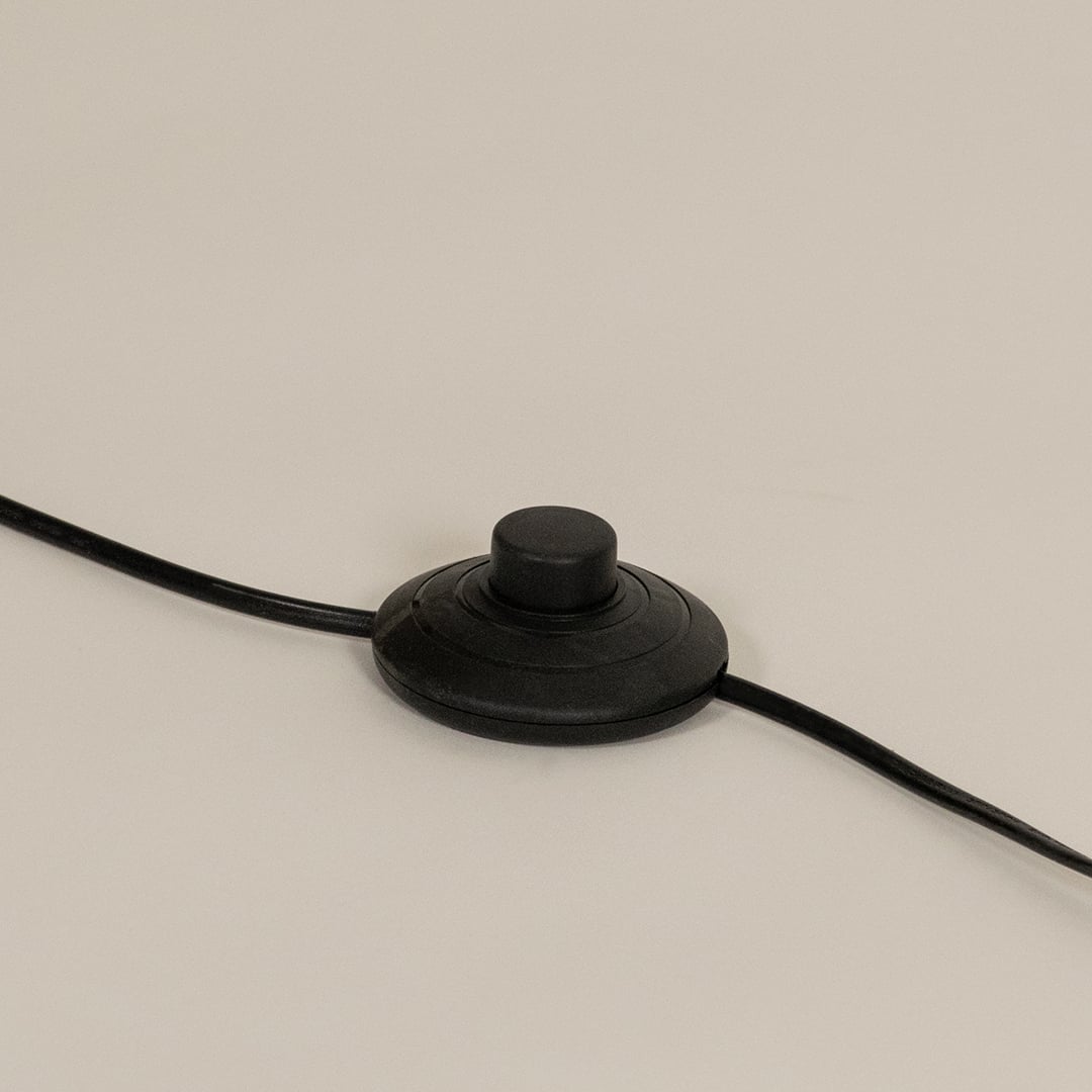 Close up of a round black foot switch attached to a floor lamp power cord resting on a light surface.