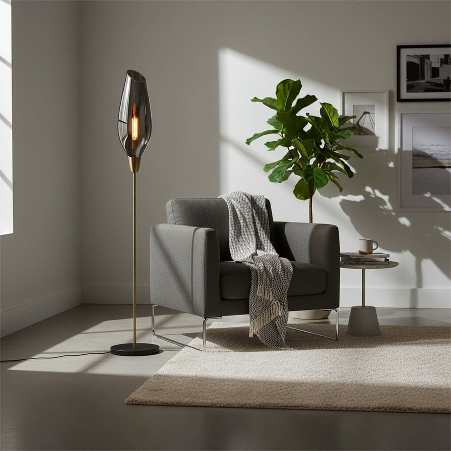 Modern floor lamp with tall smoke grey glass shade slim metal stand and round base adding warm ambient lighting to stylish contemporary interior home decor settings.