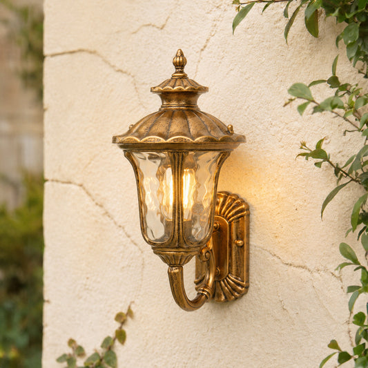 Antique brass outdoor wall lantern lifestyle image with textured glass shade mounted on a textured cream villa wall.
