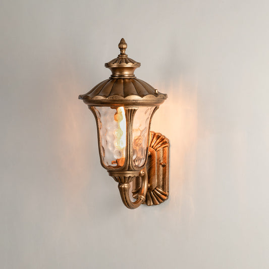 Antique brass outdoor wall light on white background with textured water glass shade for traditional porch decor.