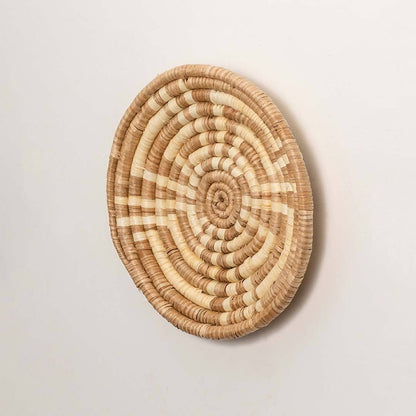 Side view of handcrafted natural brown cream woven seagrass wall basket with concentric spiral pattern for boho wall decor.