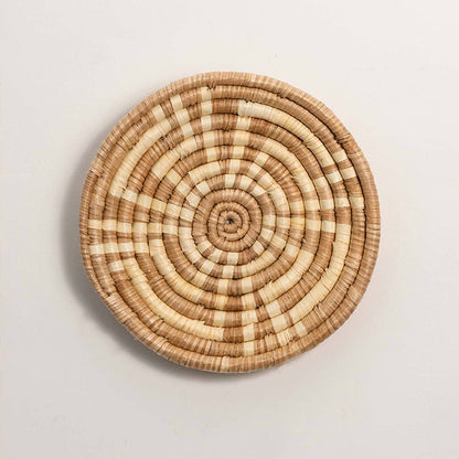 Round handcrafted natural brown cream woven seagrass wall basket with concentric spiral pattern on white background image.