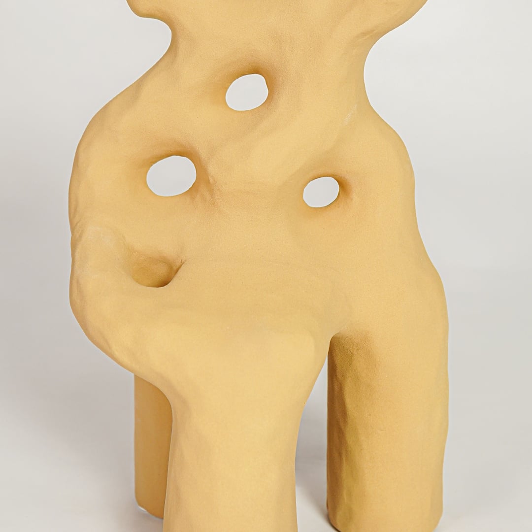 Closeup of mustard glazed ceramic vase with artistic curved silhouette ideal for elegant home decor shelf styling.