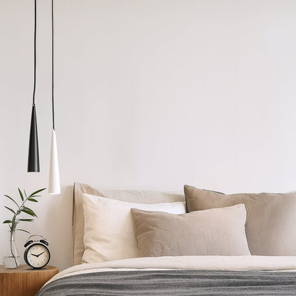 Modern cone pendant lights in black and white metal hanging above a cozy bedroom side table for stylish home lighting.