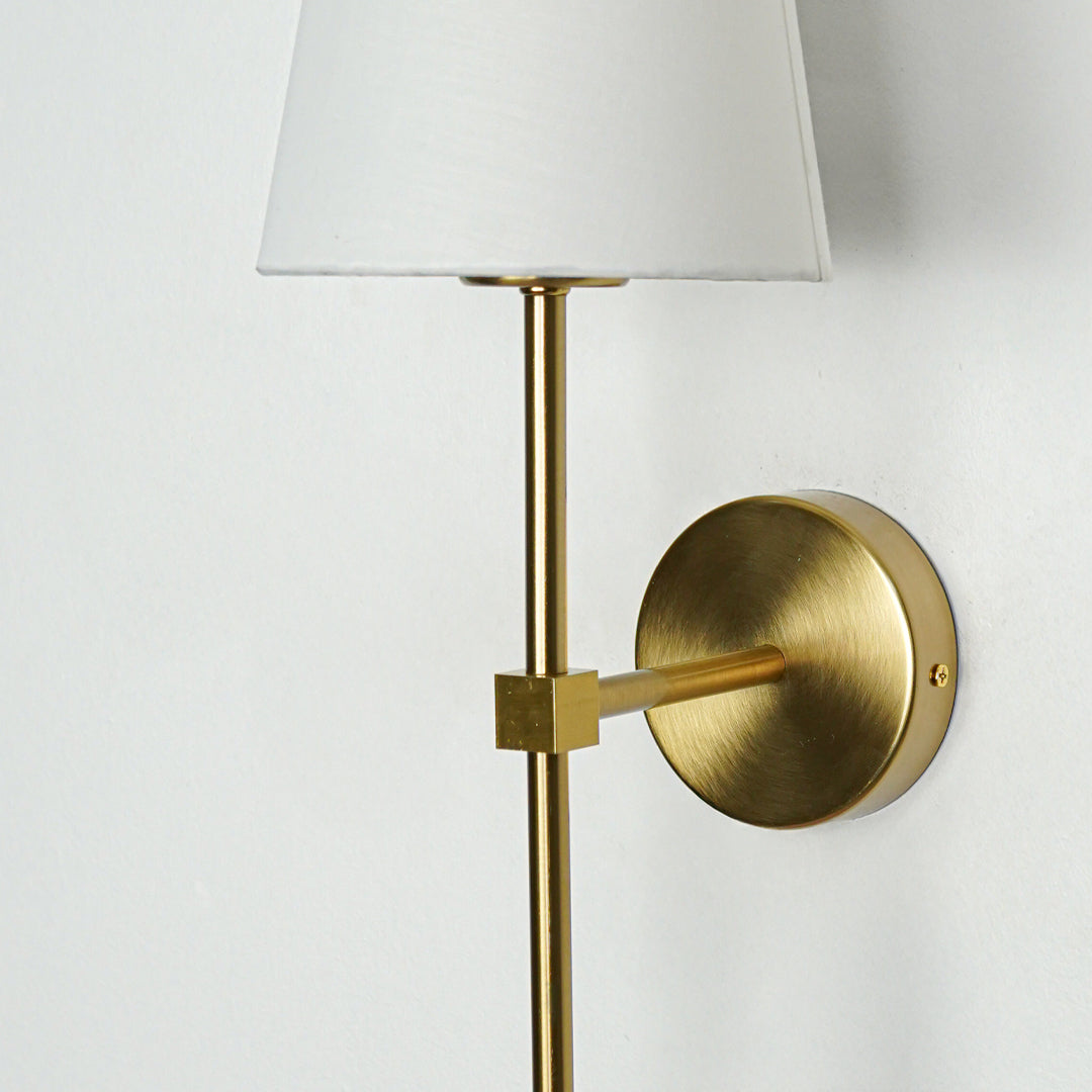 Contemporary wall light in gold metal finish with fabric shade for bedroom or living decor lighting white background.