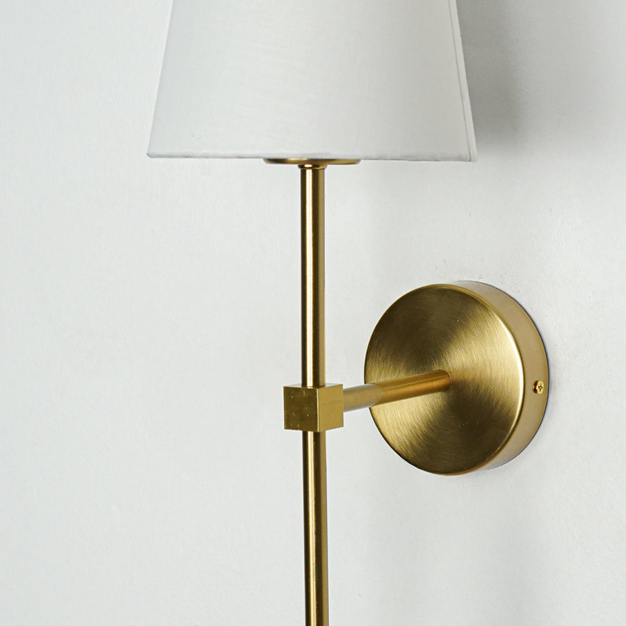 Contemporary wall light in gold metal finish with fabric shade for bedroom or living decor lighting white background.