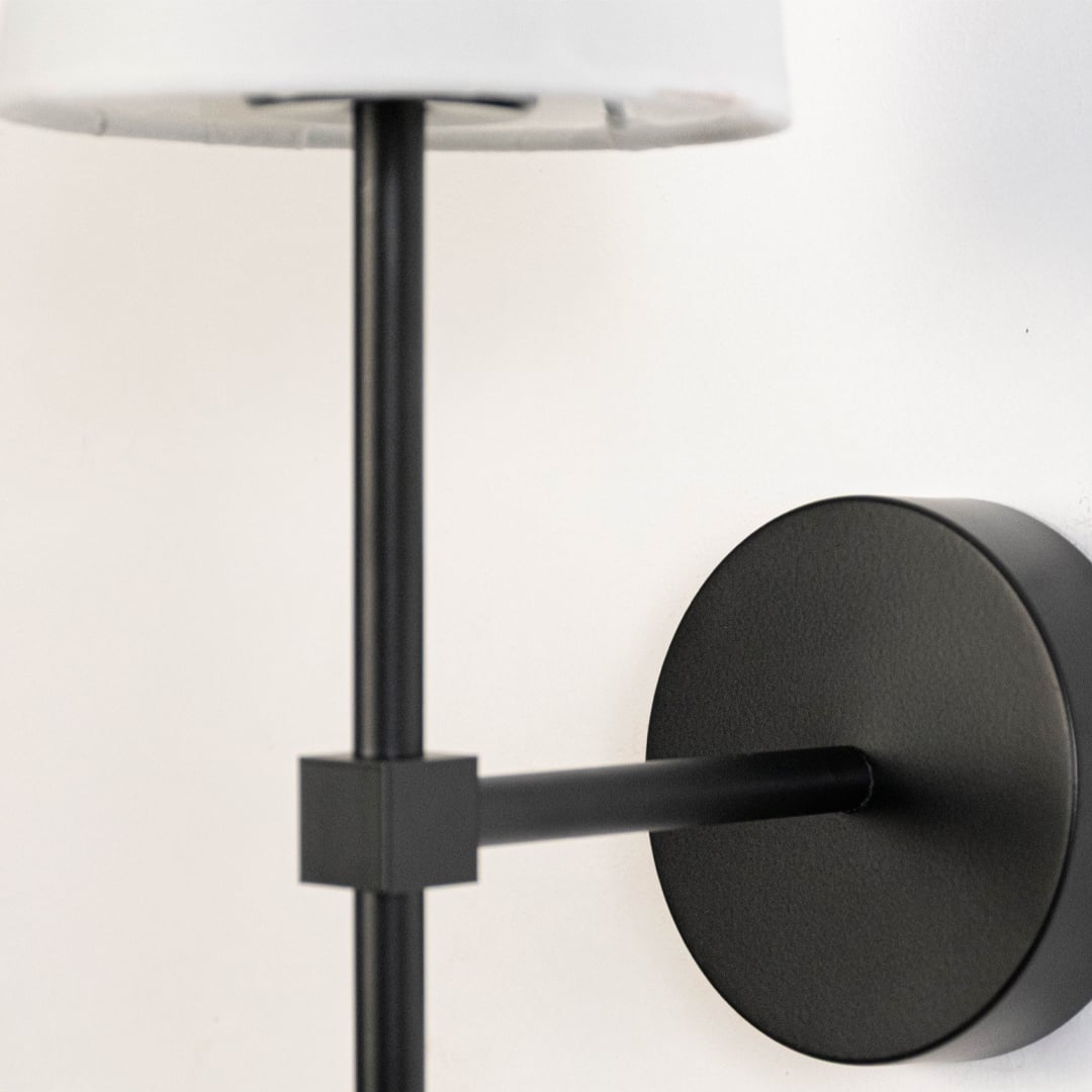 Detailed closeup of white fabric cylindrical shade and matte black metal rod hardware on contemporary minimalist wall sconce.