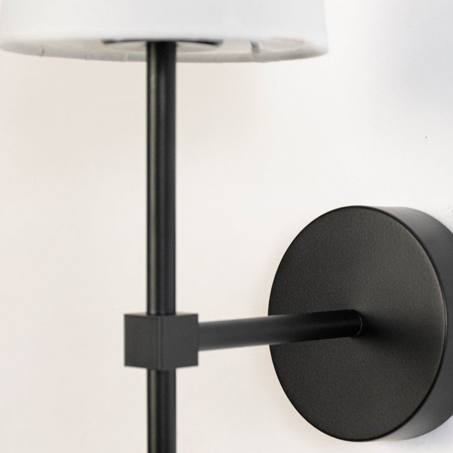 Detailed closeup of white fabric cylindrical shade and matte black metal rod hardware on contemporary minimalist wall sconce.