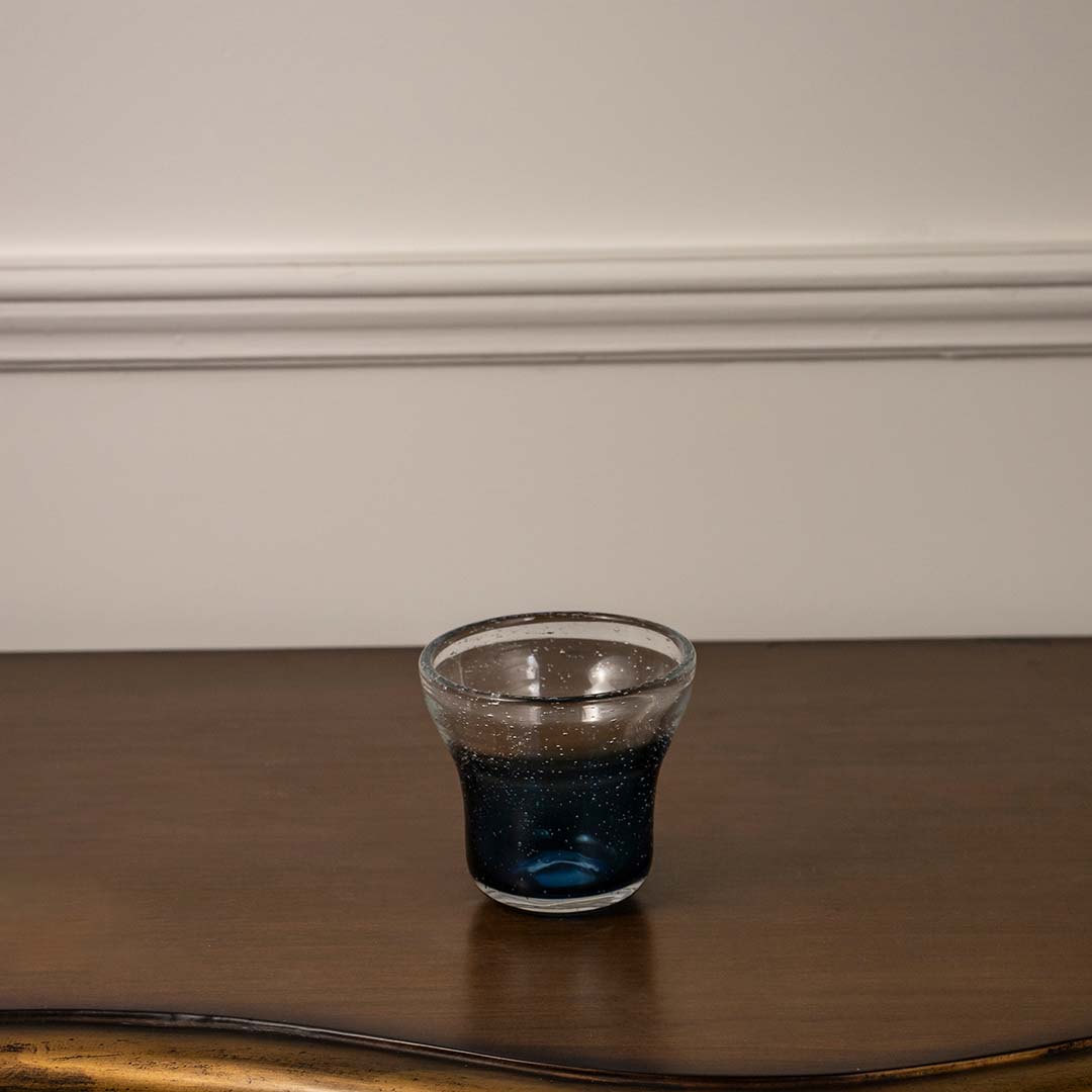 Transparent glass with deep blue base detail placed on wooden table against neutral wall background showcasing contemporary drinkware aesthetic.