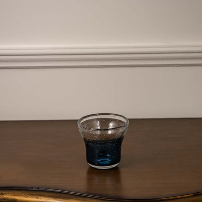 Transparent glass with deep blue base detail placed on wooden table against neutral wall background showcasing contemporary drinkware aesthetic.