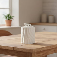 White textured ceramic decorative jar with sculpted animal lid styled on wooden table in warm modern living room setting.