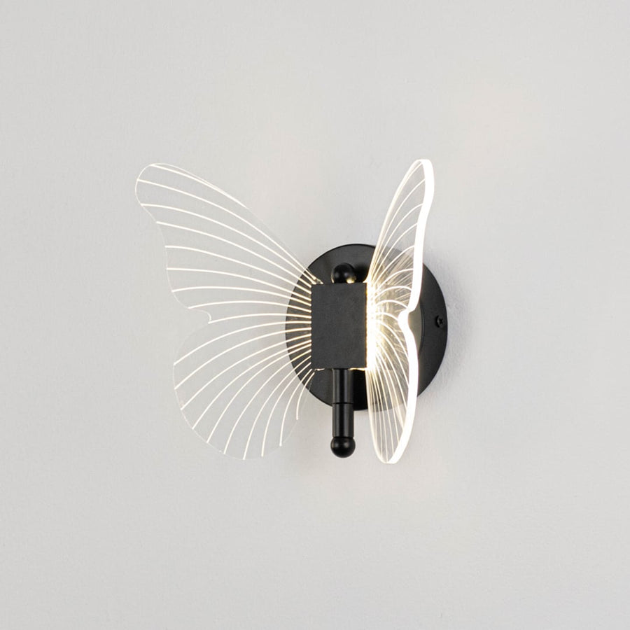 Black butterfly wall light with clear acrylic wings illuminated on a bright white background for clear visibility.