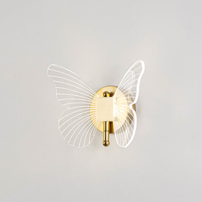 Gold butterfly wall light with clear acrylic wings illuminated on a bright white background for clear visibility.