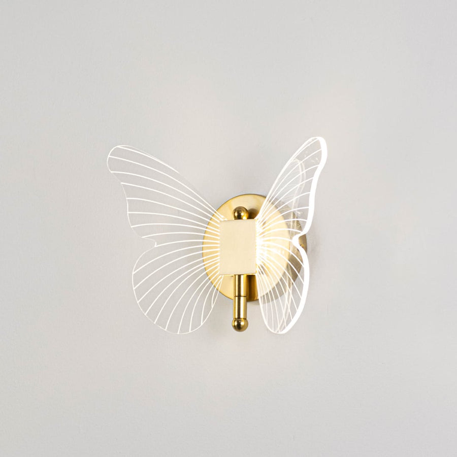 Gold butterfly wall light with clear acrylic wings illuminated on a bright white background for clear visibility.