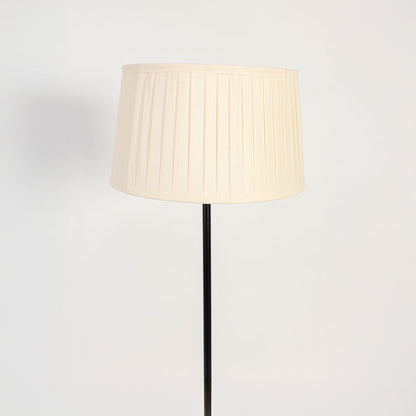 Closeup of elegant white pleated fabric shade floor lamp with slim black stand for bedroom or living room lighting.