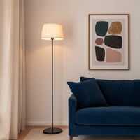 White pleated fabric shade floor lamp with slim black stand styled in modern living room beside navy sofa.