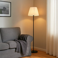 Modern floor lamp with pleated white fabric shade placed beside a grey armchair adding warm ambient lighting to a cozy living room setting with minimalist decor.