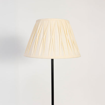 Closeup of cream pleated fabric shade and slim black stand floor lamp for stylish bedroom or living room lighting.