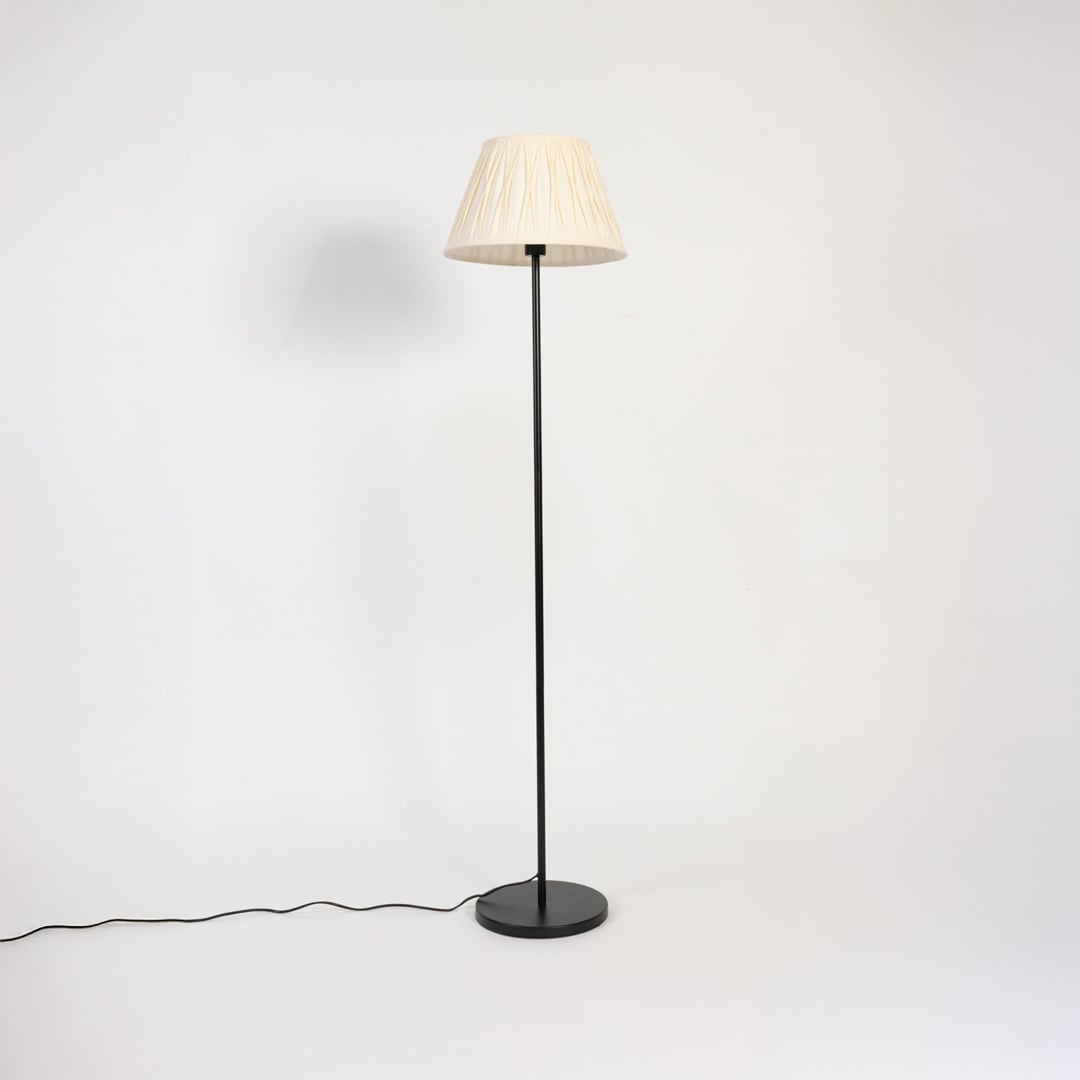 Modern cream pleated shade floor lamp with slim black stand shown switched off on white background.
