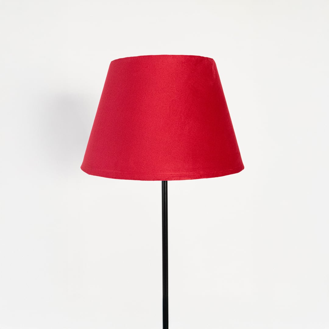 Closeup of elegant red fabric shade floor lamp with slim black metal stand for bedroom or living room lighting.