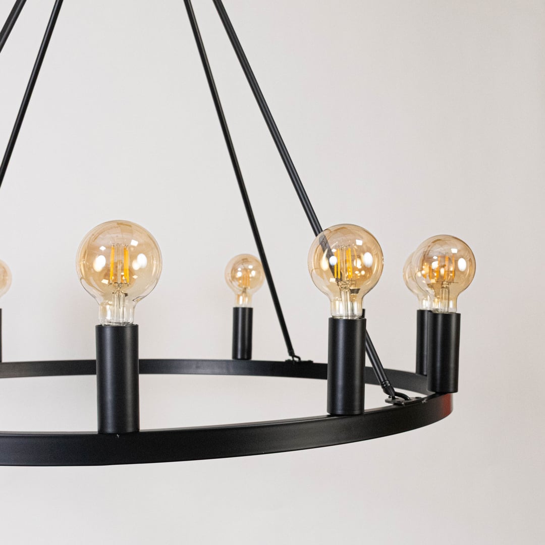 Detailed closeup of amber Edison globe bulbs with black metal cylindrical sockets on contemporary industrial chandelier frame.