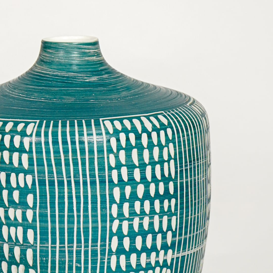 Closeup of teal glazed ceramic vase with white hand painted pattern showcasing textured finish for elegant home decor styling.