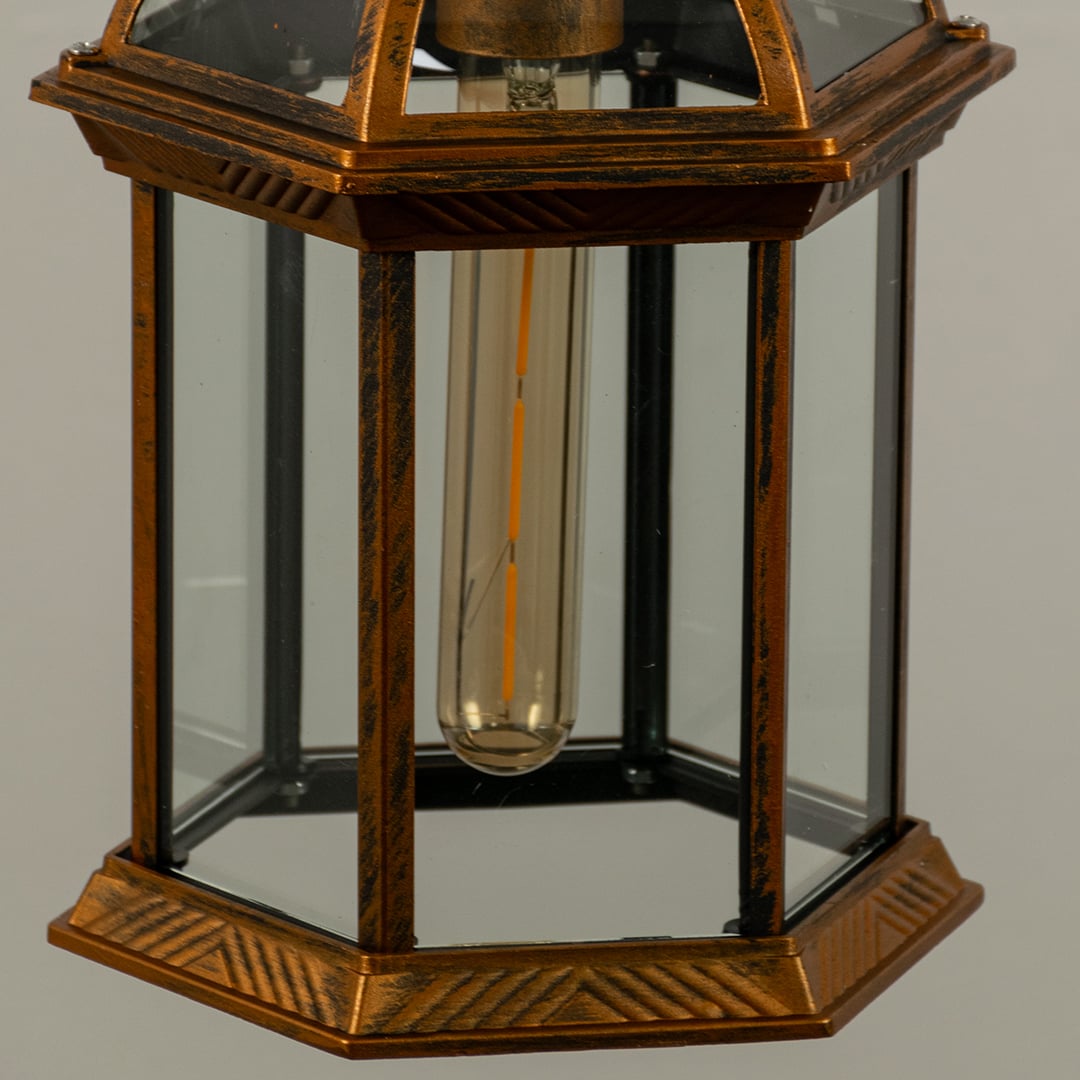 Closeup of bronze hanging lantern with warm light on showing vintage detailing clear panels and glowing filament ideal for atmospheric lighting.