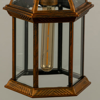 Closeup of bronze hanging lantern with warm light on showing vintage detailing clear panels and glowing filament ideal for atmospheric lighting.