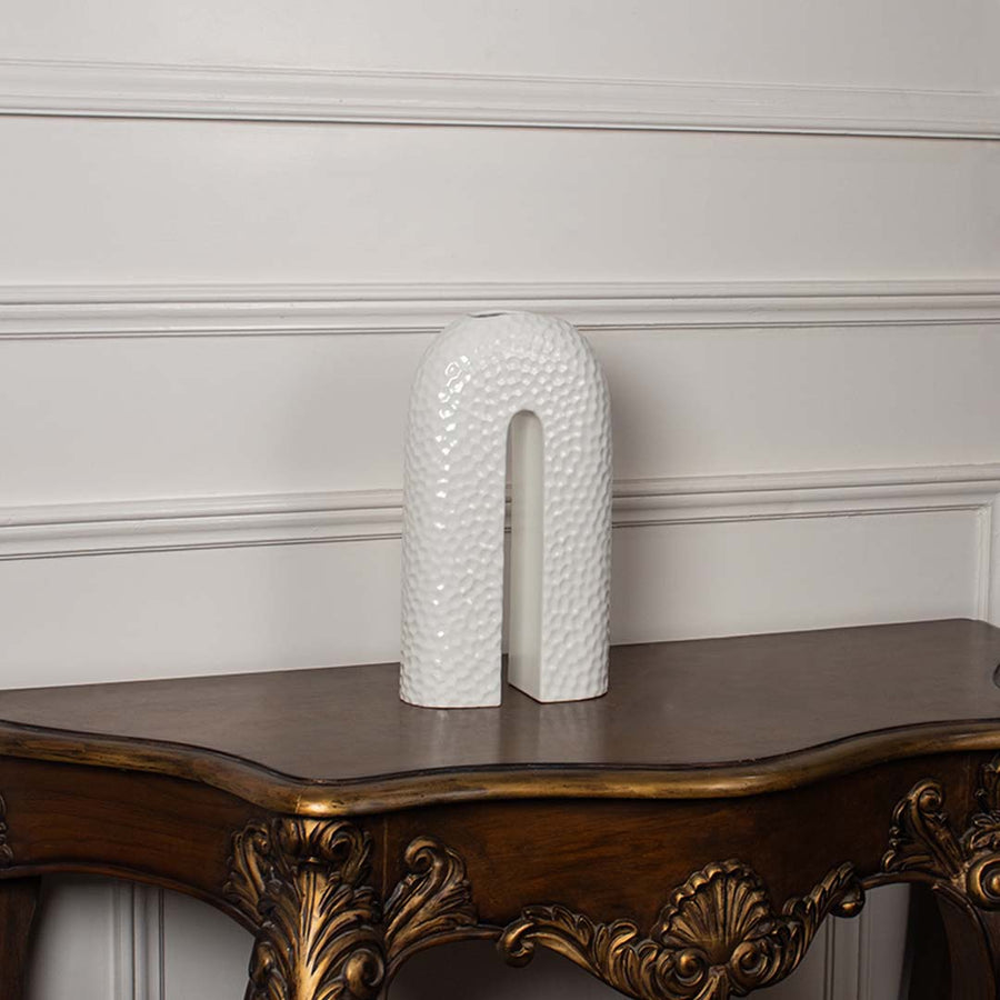 White arch shaped ceramic vase with an intricate braided rope texture displayed on a classic wooden console table for decor.