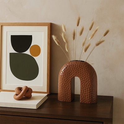 Lifestyle image of a modern brown arched ceramic vase styled in a minimal setting for a clean decorative look.
