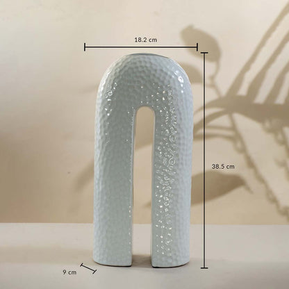 White ceramic arch-shaped vase with hammered finish shown with 38.5 cm height and 18.2 cm width measurement detail.