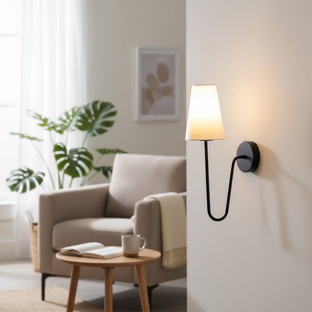 Minimalist black curved gooseneck wall lamp with a white cone shade illuminating a cozy living room armchair space.