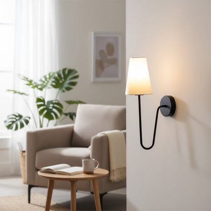 Minimalist black curved gooseneck wall lamp with a white cone shade illuminating a cozy living room armchair space.