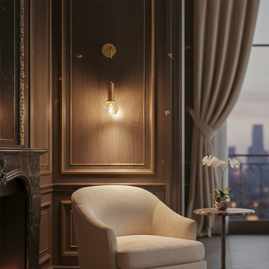 Lifestyle image of gold metal wall light with clear glass shade mounted beside lounge chair adding warm ambient lighting.