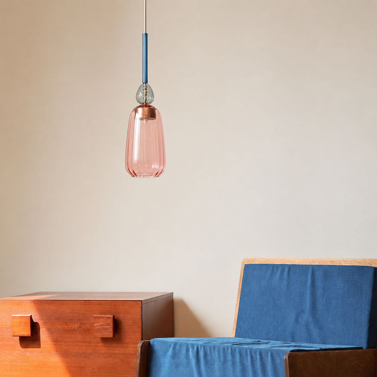 A modern pendant light with a translucent pink glass shade and a blue cord, hanging in a minimalist room above a wooden side table and a blue upholstered chair.