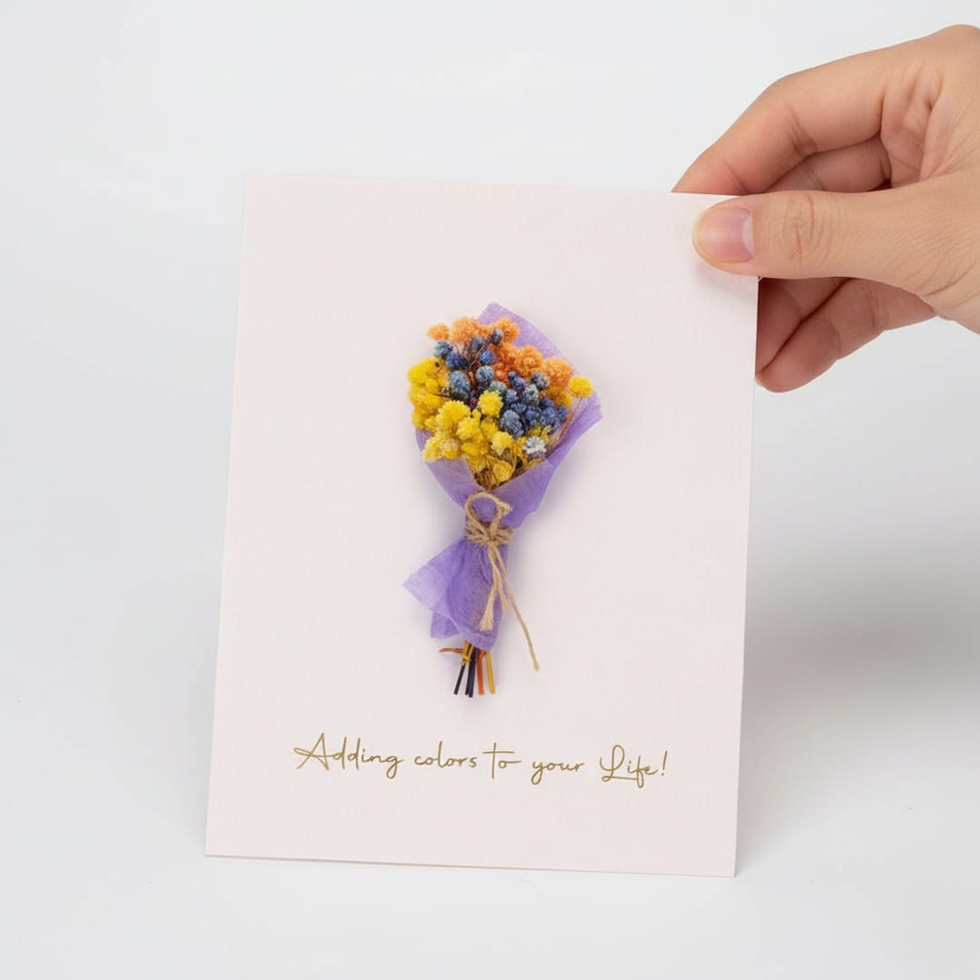 Hand holding a white greeting card featuring a colorful mini dried flower bouquet isolated on a clean white background.
