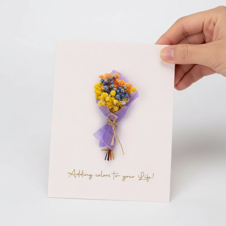Hand holding a white greeting card featuring a colorful mini dried flower bouquet isolated on a clean white background.