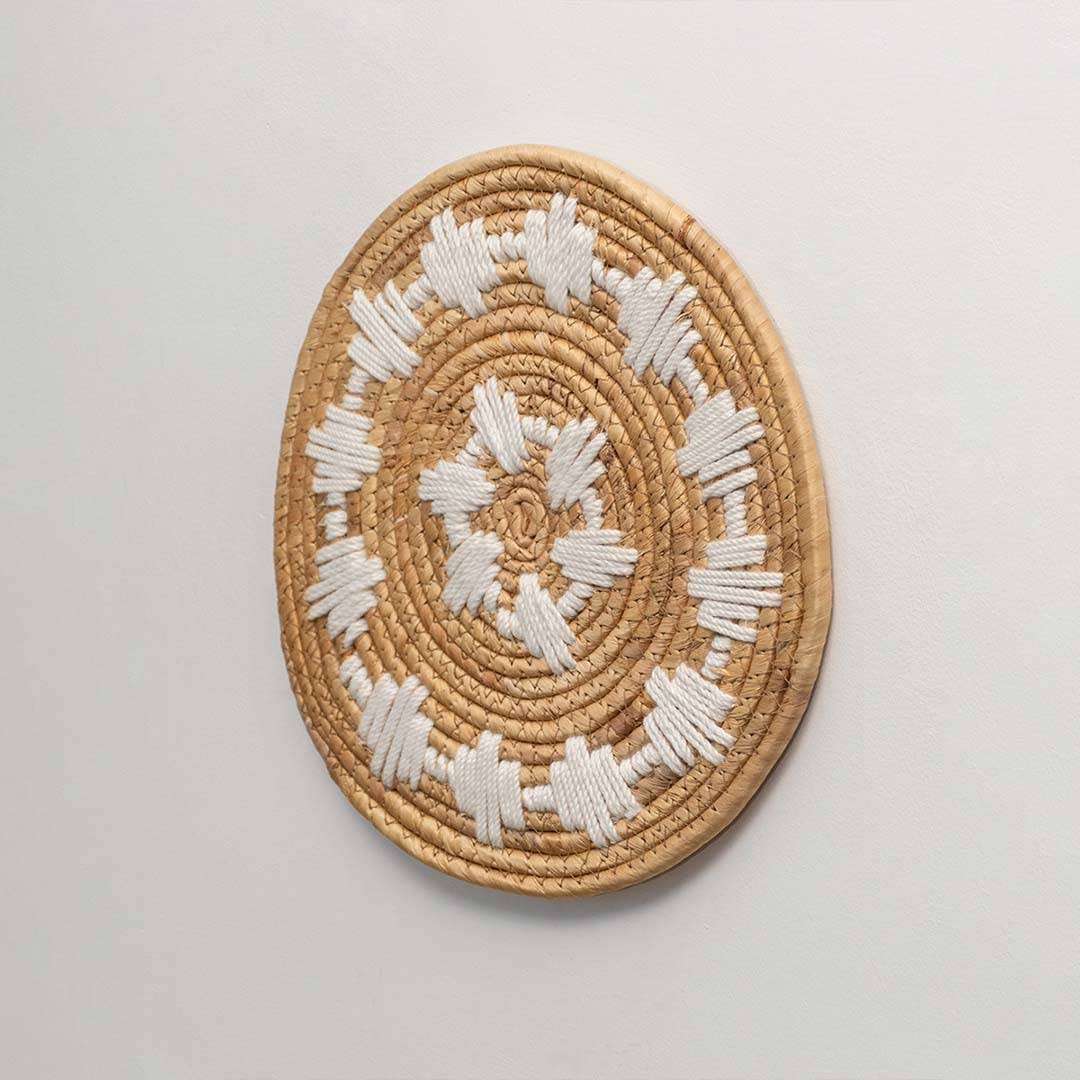 Round handcrafted natural seagrass wall basket with white sunburst pattern on white background image.