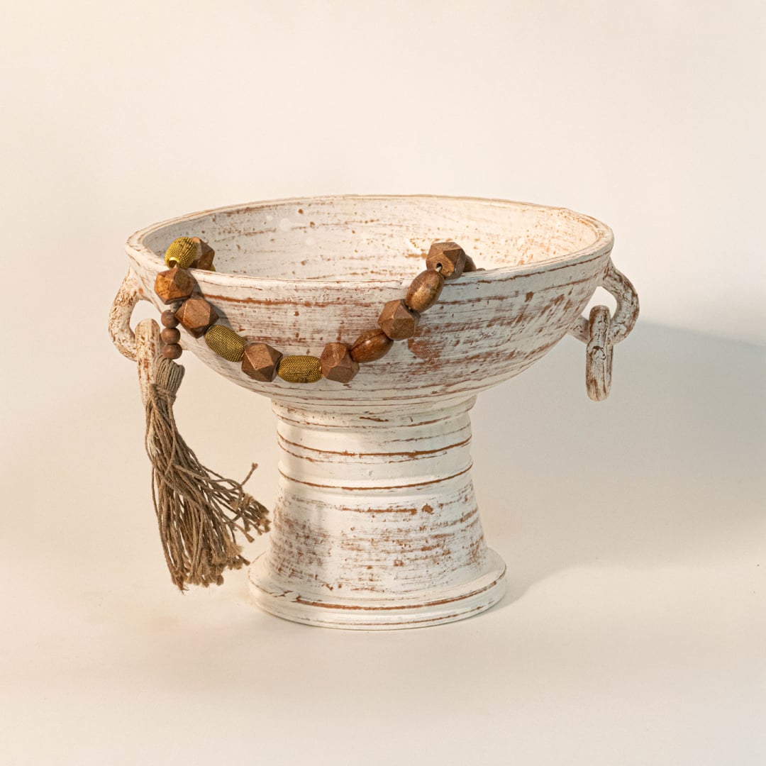 Brown bead garland draped over a white ceramic pedestal bowl for earthy bohemian home styling.