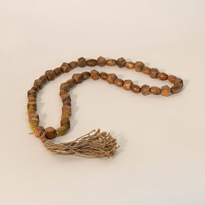 Brown bead garland displayed on off-white surface highlighting its handmade texture and neutral earthy tones.