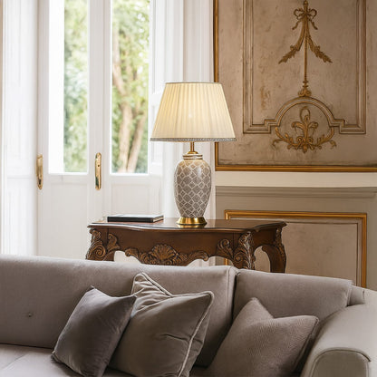 Elegant grey patterned table lamp with gold base placed on a carved wooden console in a classic living room with soft natural daylight.