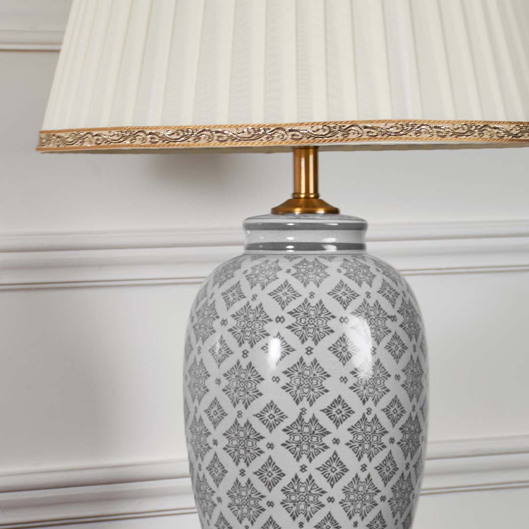 Closeup of the grey ceramic lamp body showing intricate geometric patterns and gold detailing beneath a pleated cream lampshade.